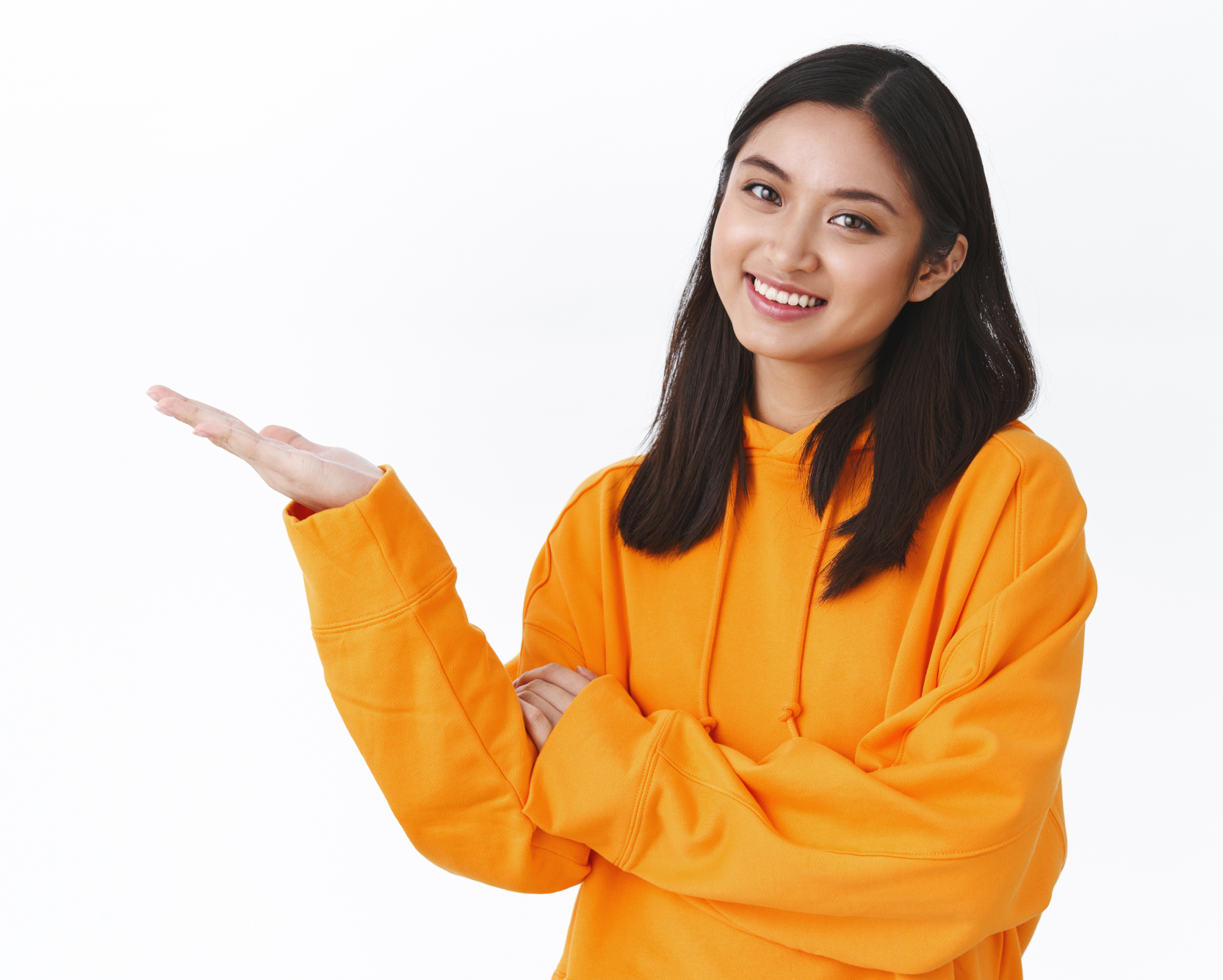 Waist-up portrait cute beautiful asian woman in orange hoodie, introduce produce banner, pointing at blank white space, holding product and smiling, recommend advertisement, white background.